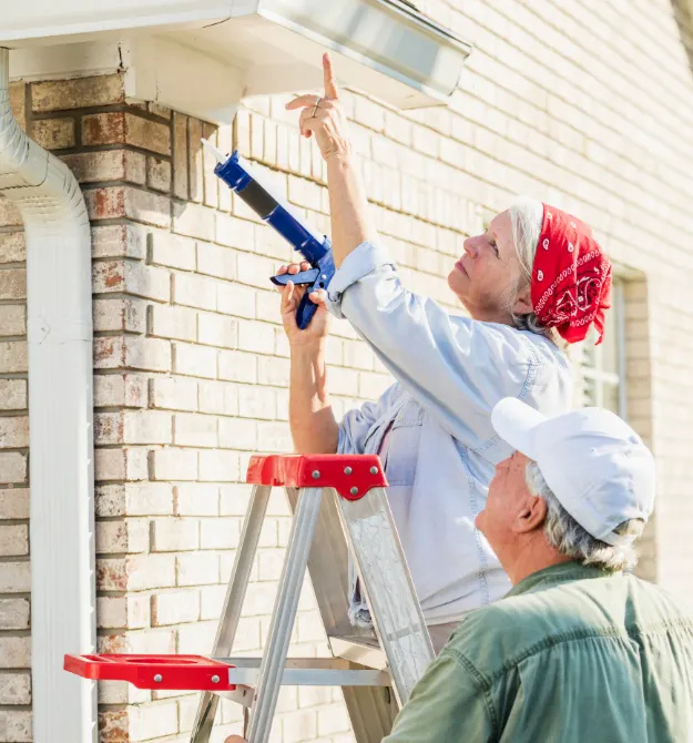 Older couple using a ladder for home repairs.