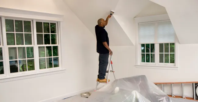Man painting a ceiling using a ladder.