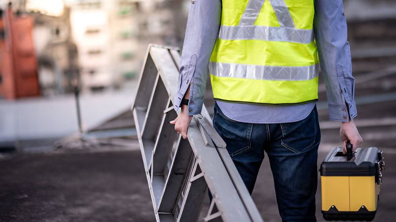 Safety worker preparing for maintenance with ladder and tools