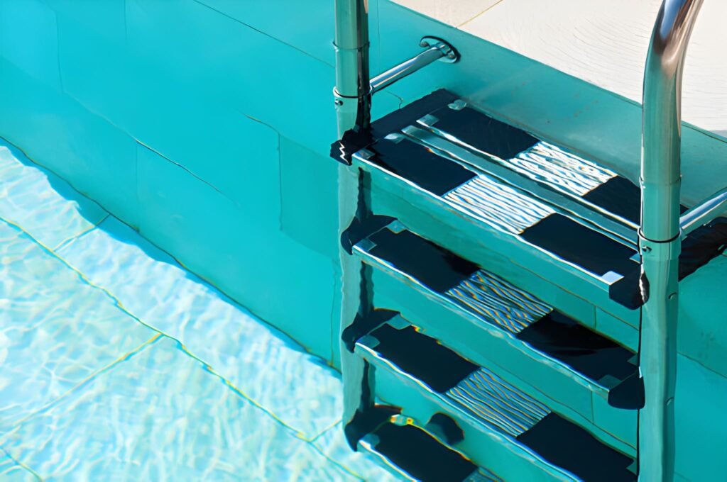 Close-up of a metal pool ladder descending into clear turquoise water with sunlight creating ripples on the pool floor.